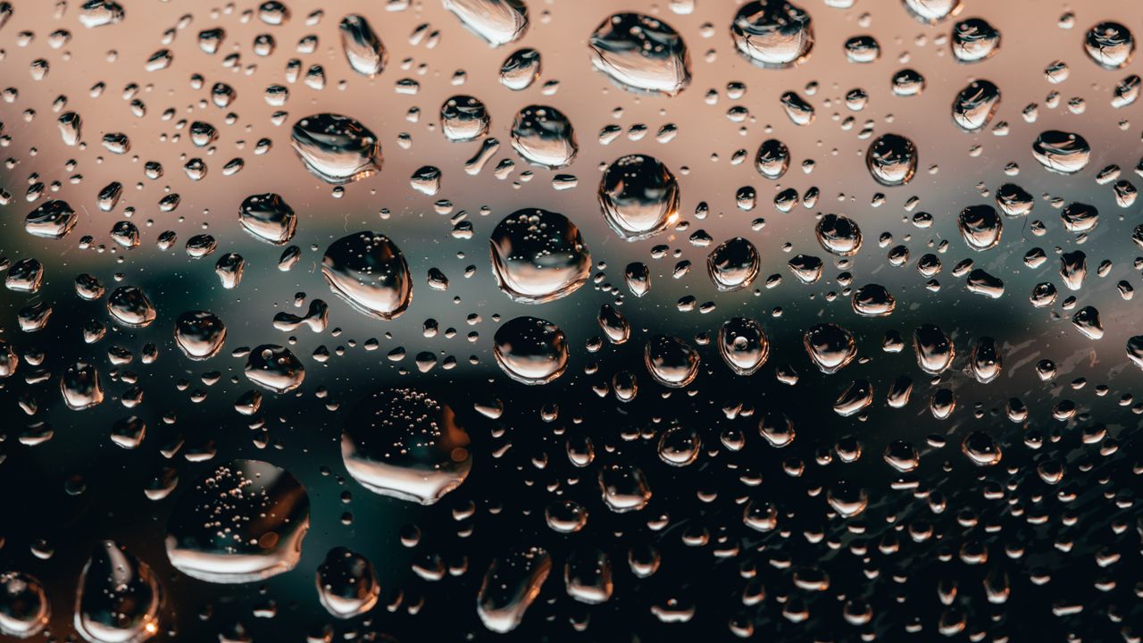 Macro shot of raindrops on a glass window with a colorful blurred background, creating a unique artistic effect.