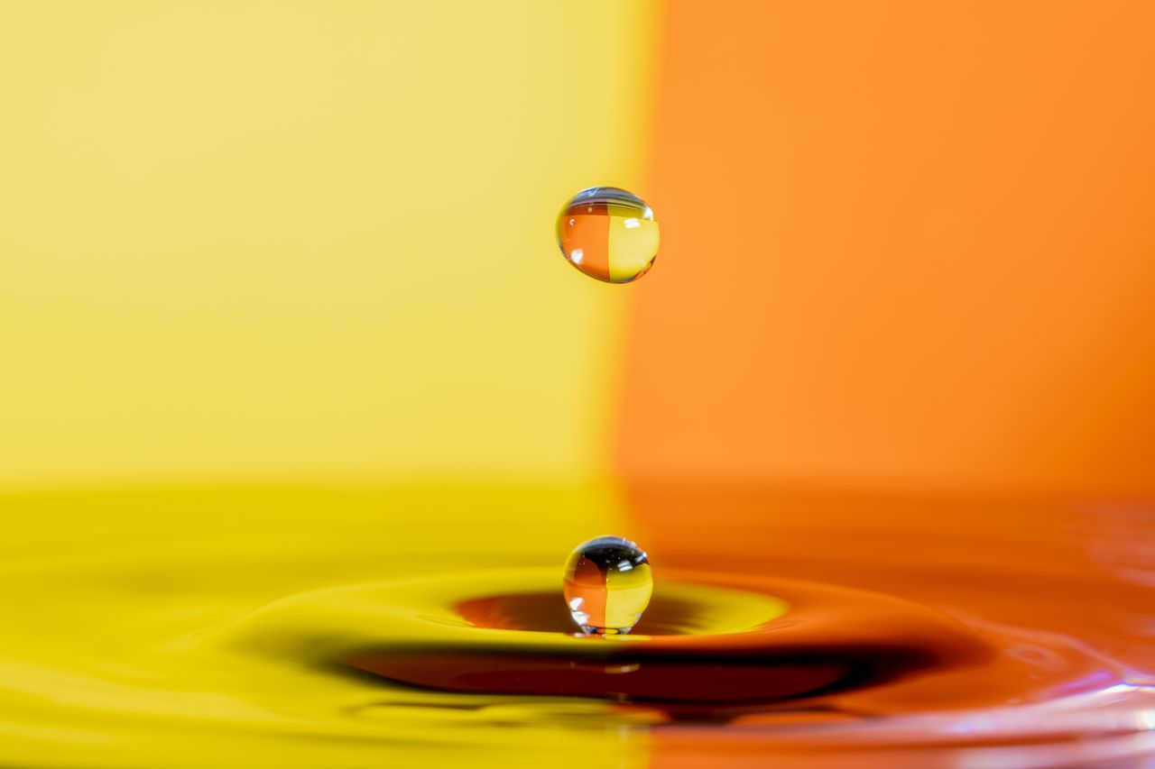 Macro shot of a water drop creating ripples against a vibrant yellow and orange background.